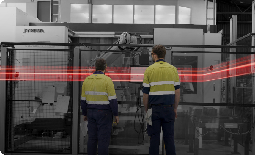 two men with their backs to the camera working in a warehouse with a machine